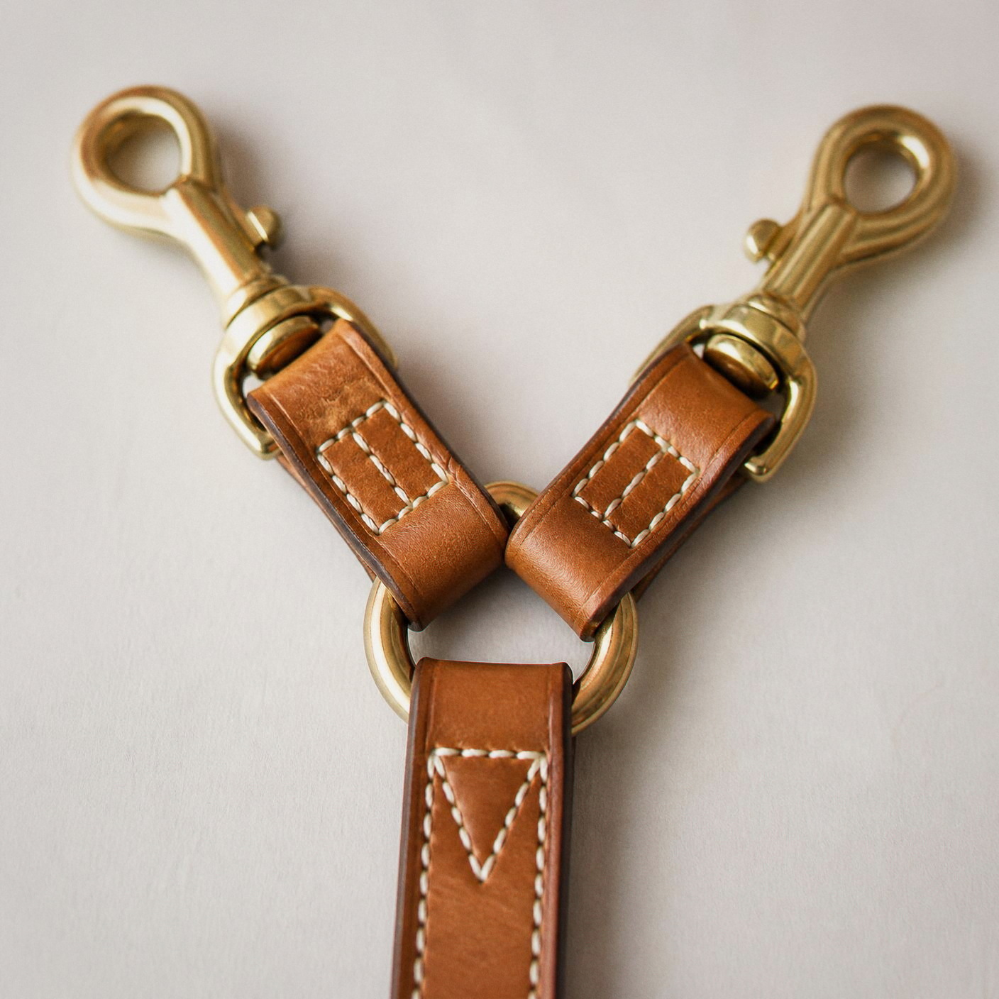 The leather junction at the hip: two hand-polished brass snap hooks, a brass ring and three saddle-stitched tabs.