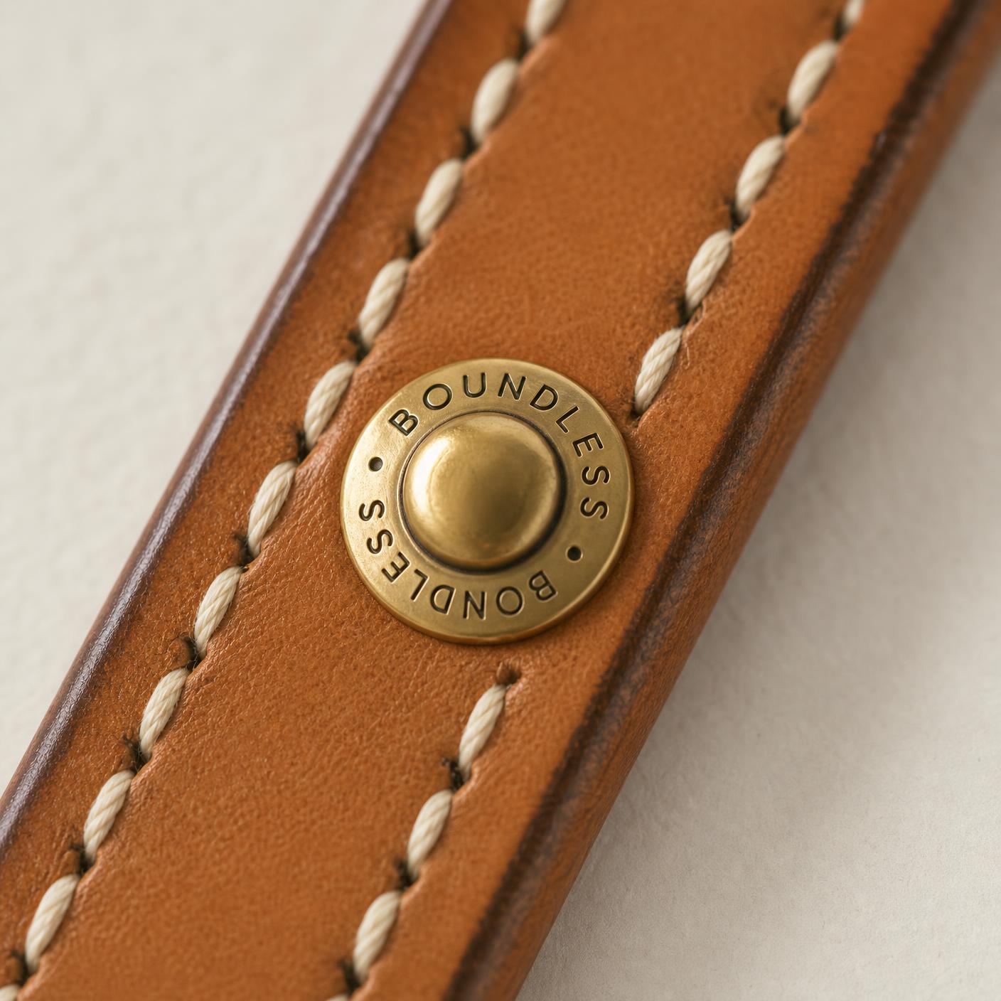 Macro detail of the brass Clou de Selle stud engraved BOUNDLESS on natural bridle leather.