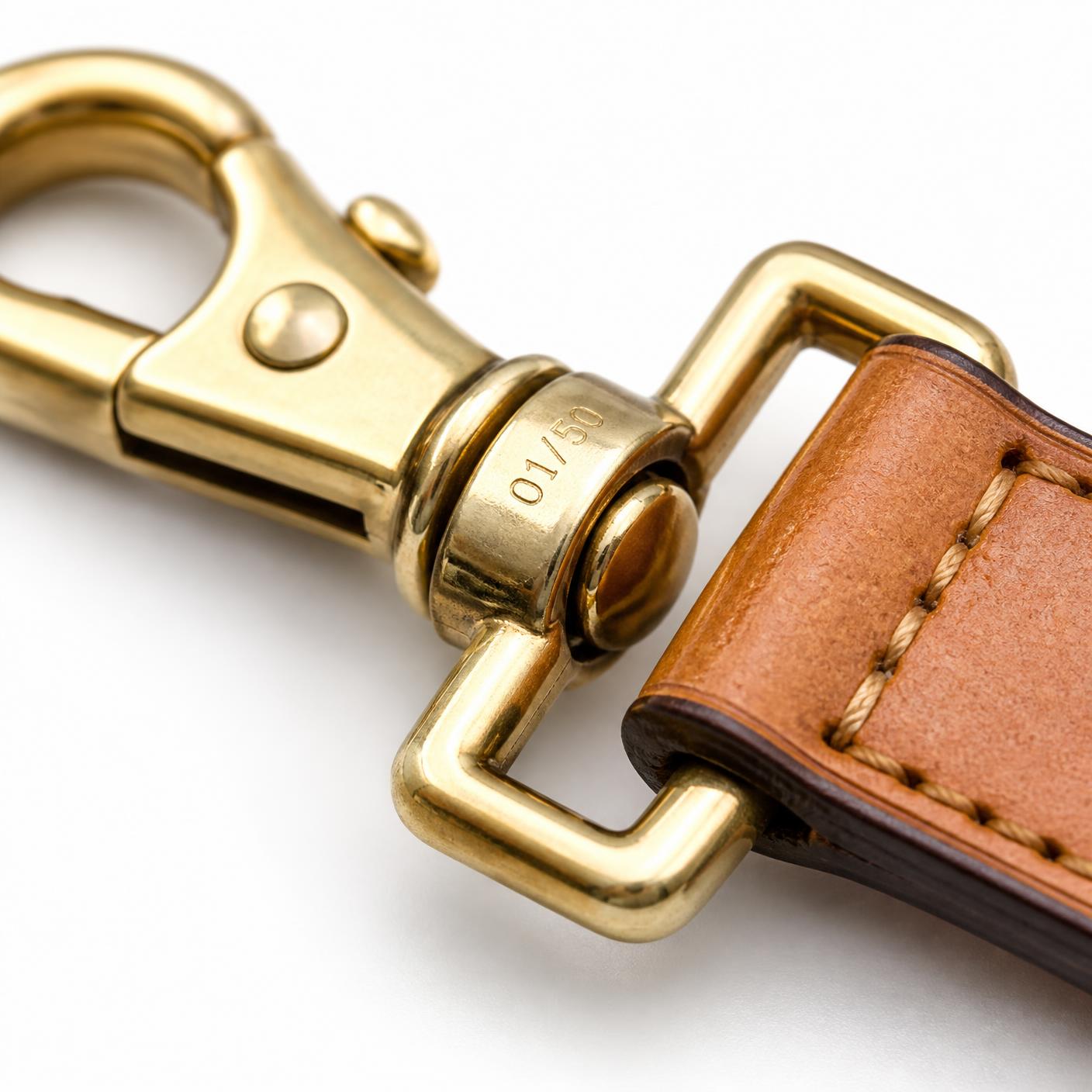 Macro detail of the solid brass swivel clip, engraved 01 of 50 on the collar, stitched onto the leather strap.