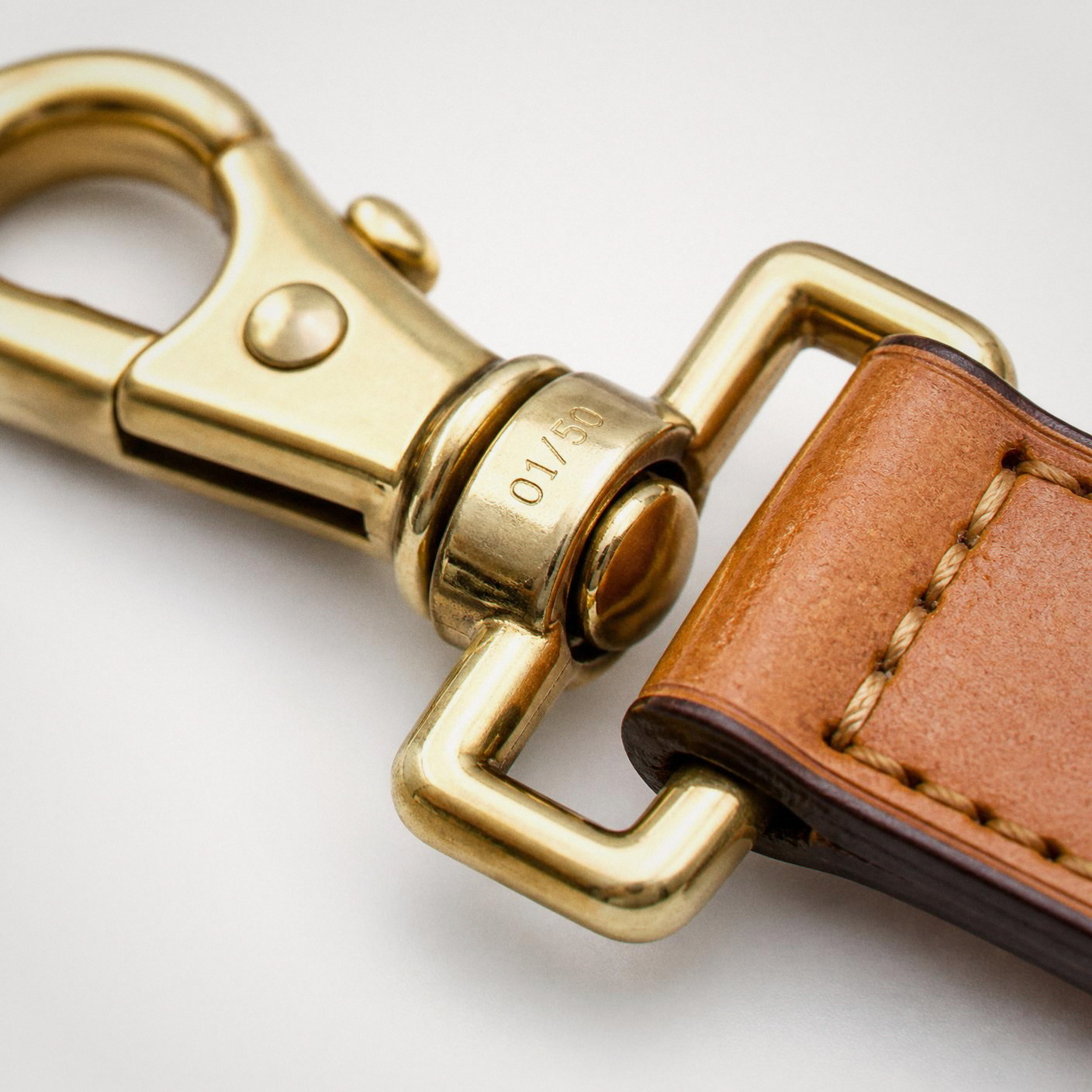 The solid brass swivel clip, engraved 01 of 50 on the collar, stitched onto the strap.
