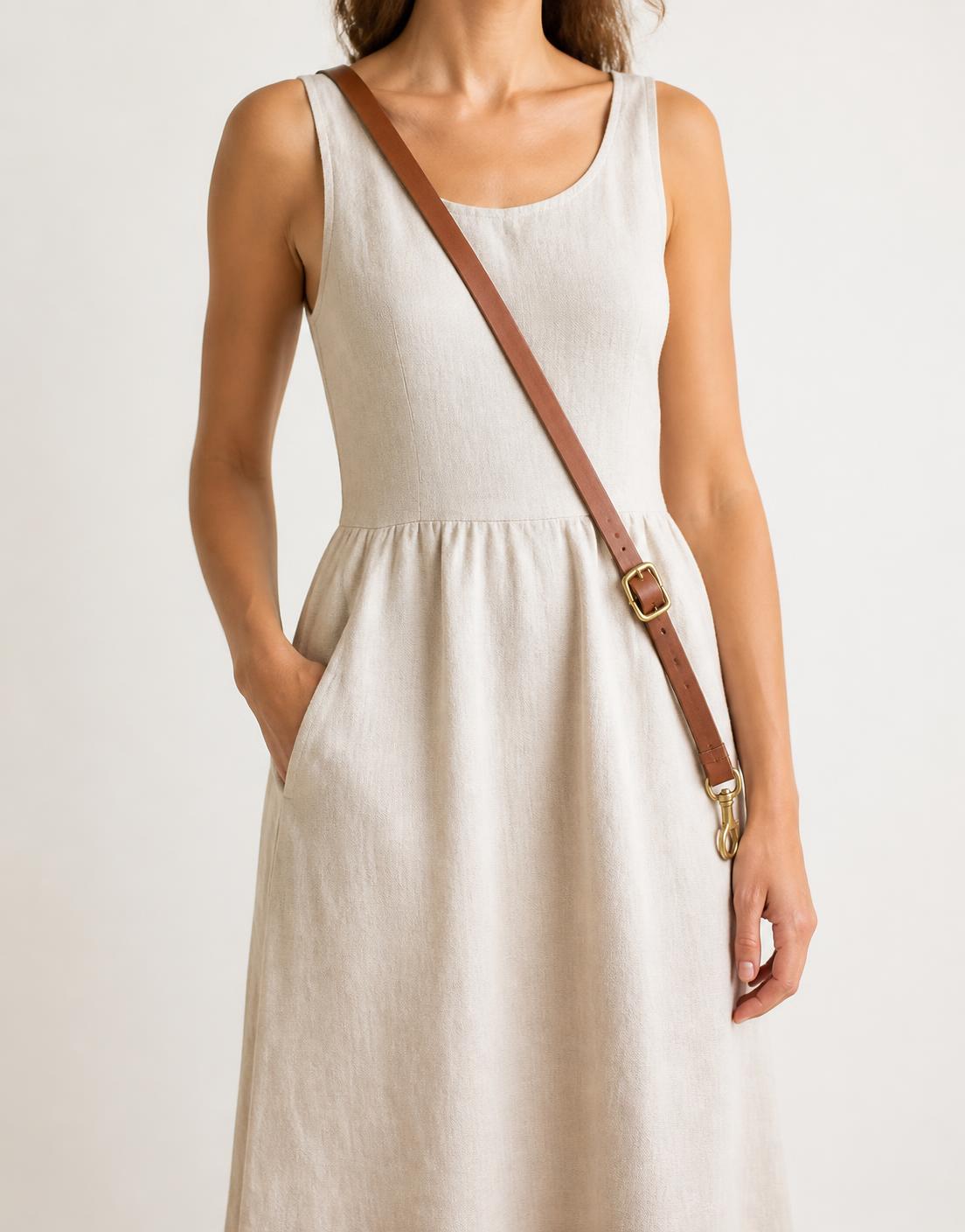 The leash worn across the body from shoulder to opposite hip over an ecru linen dress, brass buckle at the hip, clip hanging free.