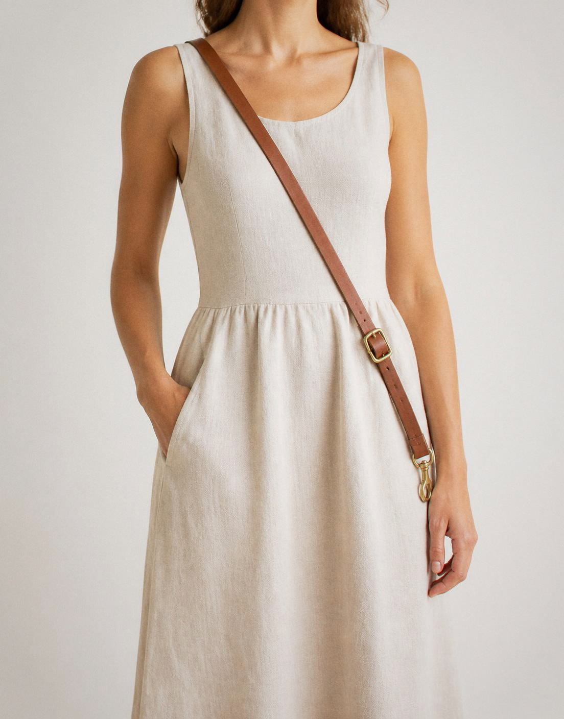 The leash worn across the body from shoulder to opposite hip over an ecru linen dress, brass buckle at the hip, clip hanging free.
