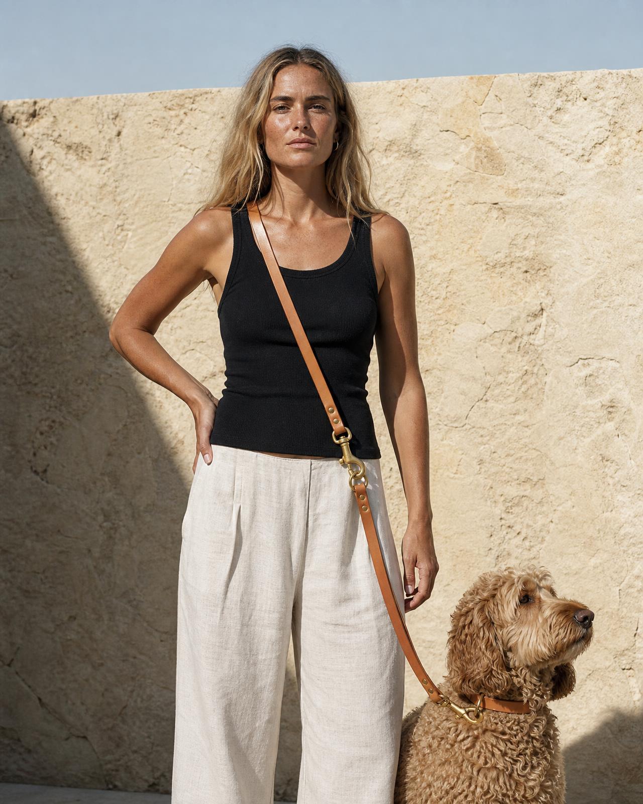 A woman on warm sandstone in morning light, the leash worn across her body, her spoodle beside her