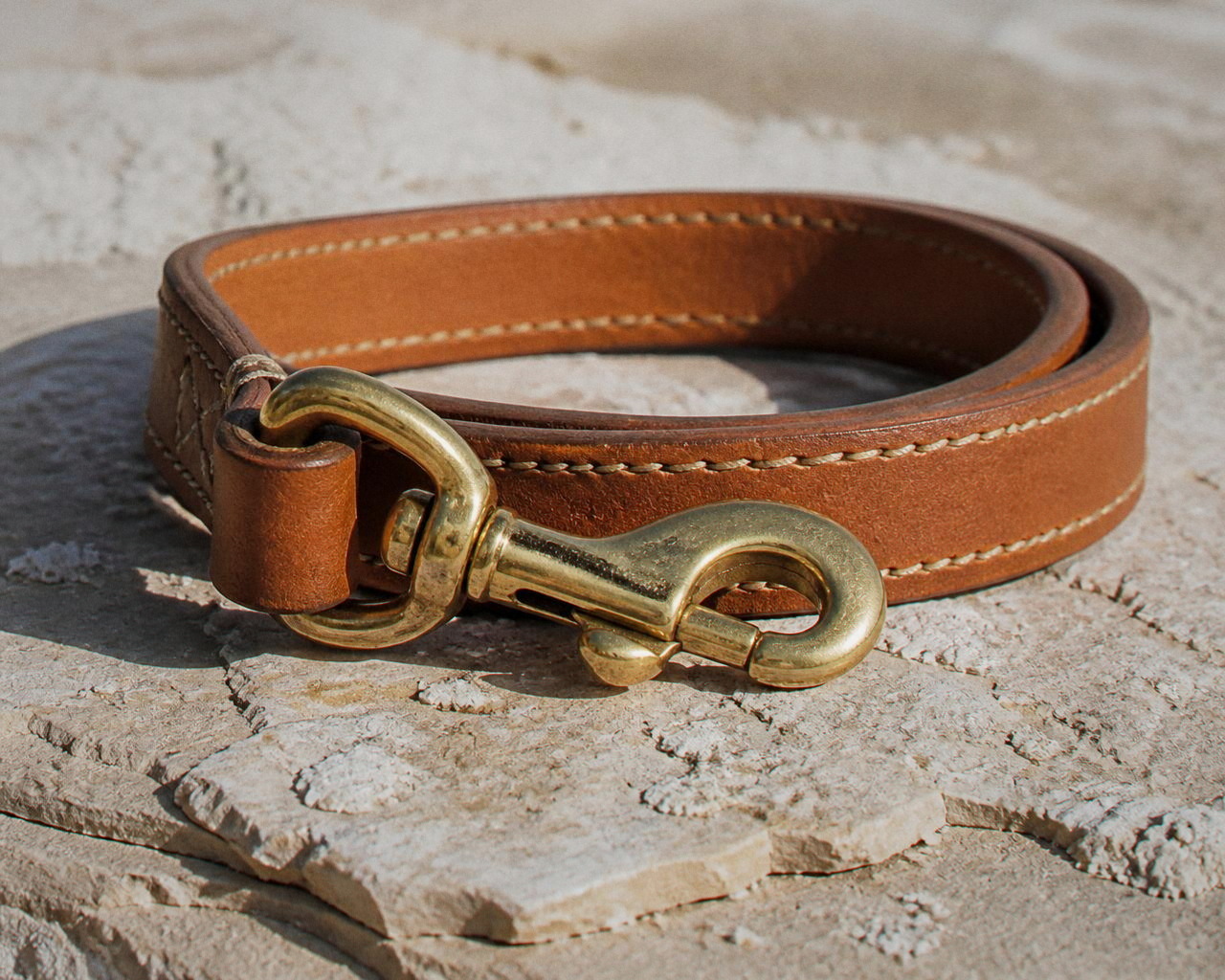 The polished brass snap closed through the ring on cognac leather with ivory stitching.